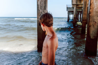 Rear view of shirtless boy standing on beach