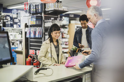 Smiling female customer buying appliance while mature owner scanning in electronics store