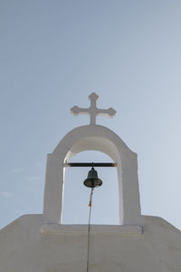 Low angle view of the bell and cross on a church in ana mera, mykonos, greece.