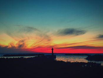 Silhouette lighthouse by sea against sky during sunset