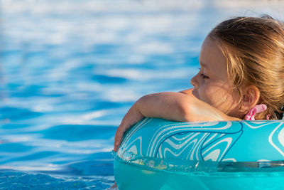 Cute little girl in blue inflatable circle swims in the pool