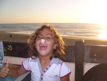 Portrait of cheerful girl with food on nose at outdoor restaurant against sea