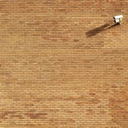 Low angle view of security camera on brick wall during sunny day