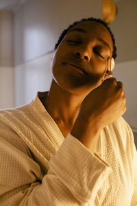 Woman with eyes closed using jade roller on face in bathroom