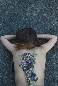 High angle view of woman lying with flowers on her back
