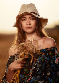 Portrait of beautiful young woman wearing hat holding plants