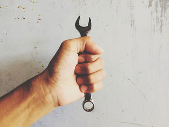 Close-up of hand holding metal against wall