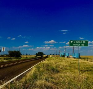 Road sign on field against blue sky