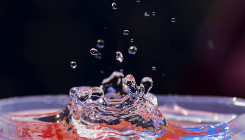 Close-up of drop falling on glass against black background