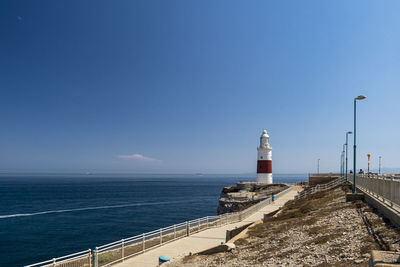 Lighthouse by sea against clear blue sky