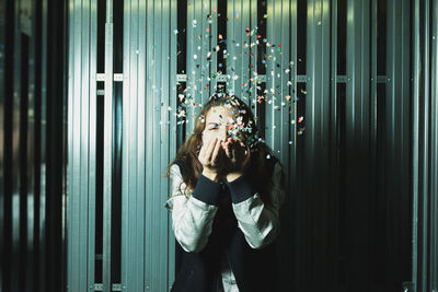 Woman blowing confetti against wall