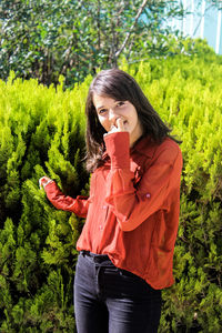 Full length of young woman standing by plants against trees