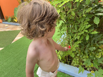 Rear view of shirtless boy standing by plants