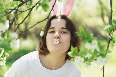 Funny teen girl with bunny ears on easter egg hunt in sunny spring garden