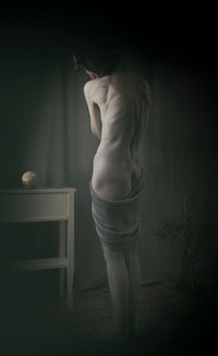 Rear view of woman standing against wall at home