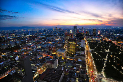 High angle view of illuminated city buildings against sky during sunset