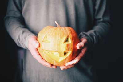 Close-up of man holding pumpkin against orange background