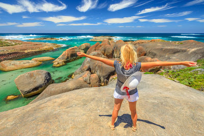 Rear view of man standing on rock by sea against sky