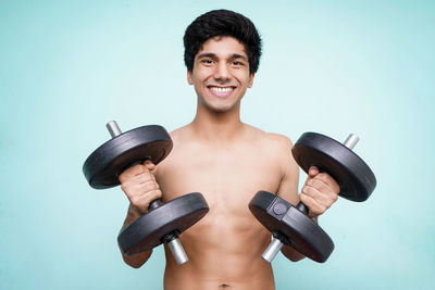 Portrait of shirtless man holding camera against gray background