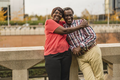 Smiling woman embracing man leaning on wall