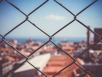 Cityscape seen through chainlink fence against sky