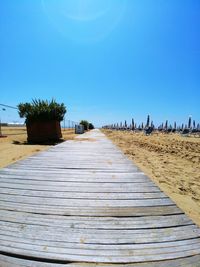 Boardwalk leading towards beach against clear blue sky