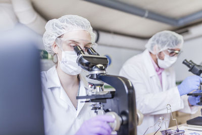 Woman and man scientists looking through microscope at laboratory