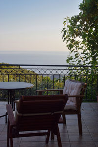 Empty chairs and table by sea against sky