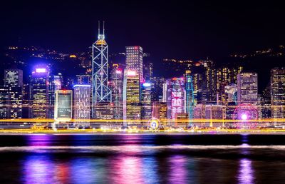 Illuminated buildings by river against sky at night