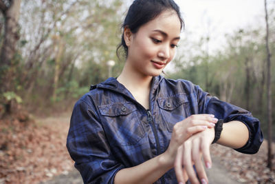 Close-up of woman checking time while standing against trees