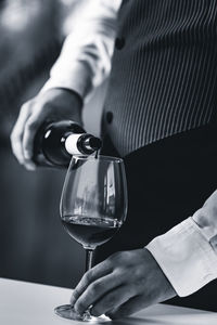 Midsection of bartendar pouring wine in glass