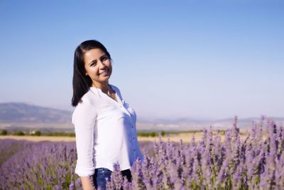 Young woman standing on field against sky