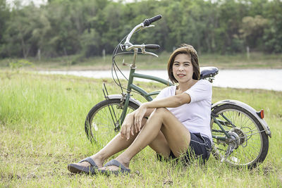 Portrait of young woman sitting on bicycle in field