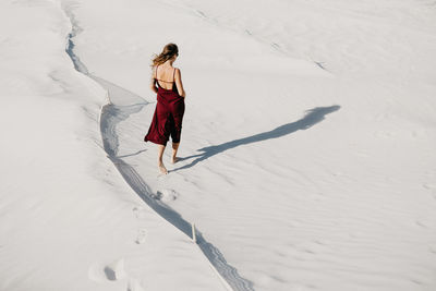 Rear view full length of young woman walking at sandy beach on sunny day