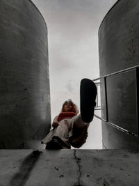 Rear view of woman sitting on wall against sky