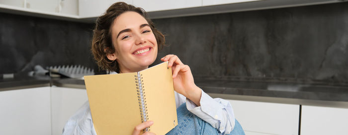 Portrait of young woman holding book at home