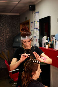 Hairdresser combs a client with a face shield in her salon