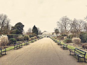 Empty park bench by trees against sky