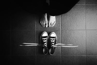 Low section of person standing in front of shoes on tiled floor