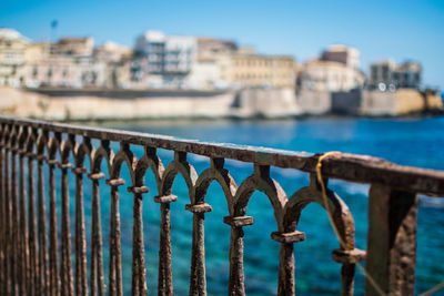 Metal fence by sea against buildings