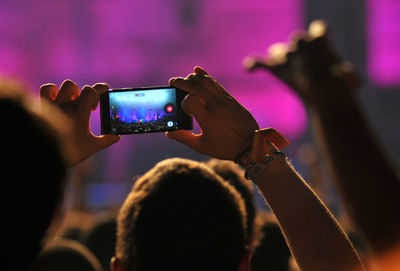 Rear view of hands holding smartphone at concert