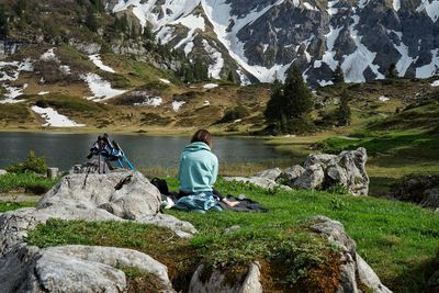 Rear view of woman sitting on rock looking at mountain by the lake in austrian alps