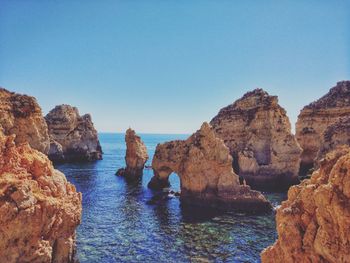 Rock formations in sea against clear blue sky