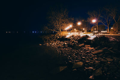 Illuminated street amidst trees against sky at night