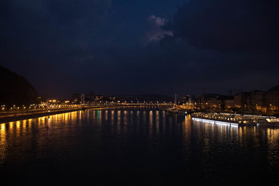 Illuminated city by river against sky at night