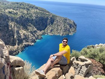 Man sitting on rock beside blue ocean at turkey on vacation trip 