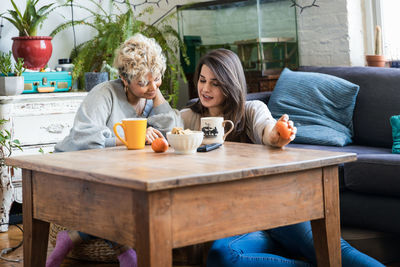 Female friends looking at mobile phone while having coffee at table in living room