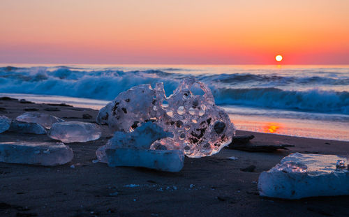 Ice at beach against orange sky during sunset