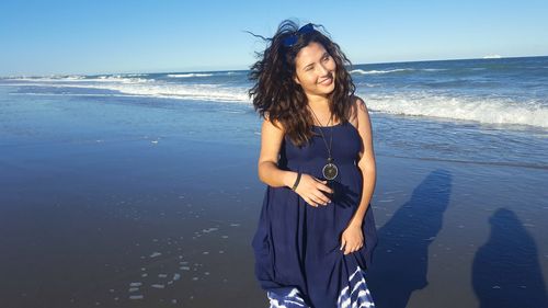 Young woman standing at beach against sky