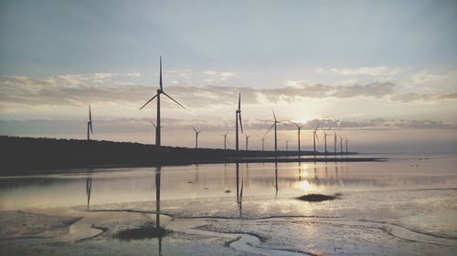 Wind turbines in lake against sky during sunset